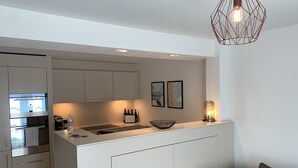 A modern kitchen with white cabinetry, a built-in stove, and a dining area with a gray sofa. - Zürich Niederdorf - Grossmünster (Zürich)