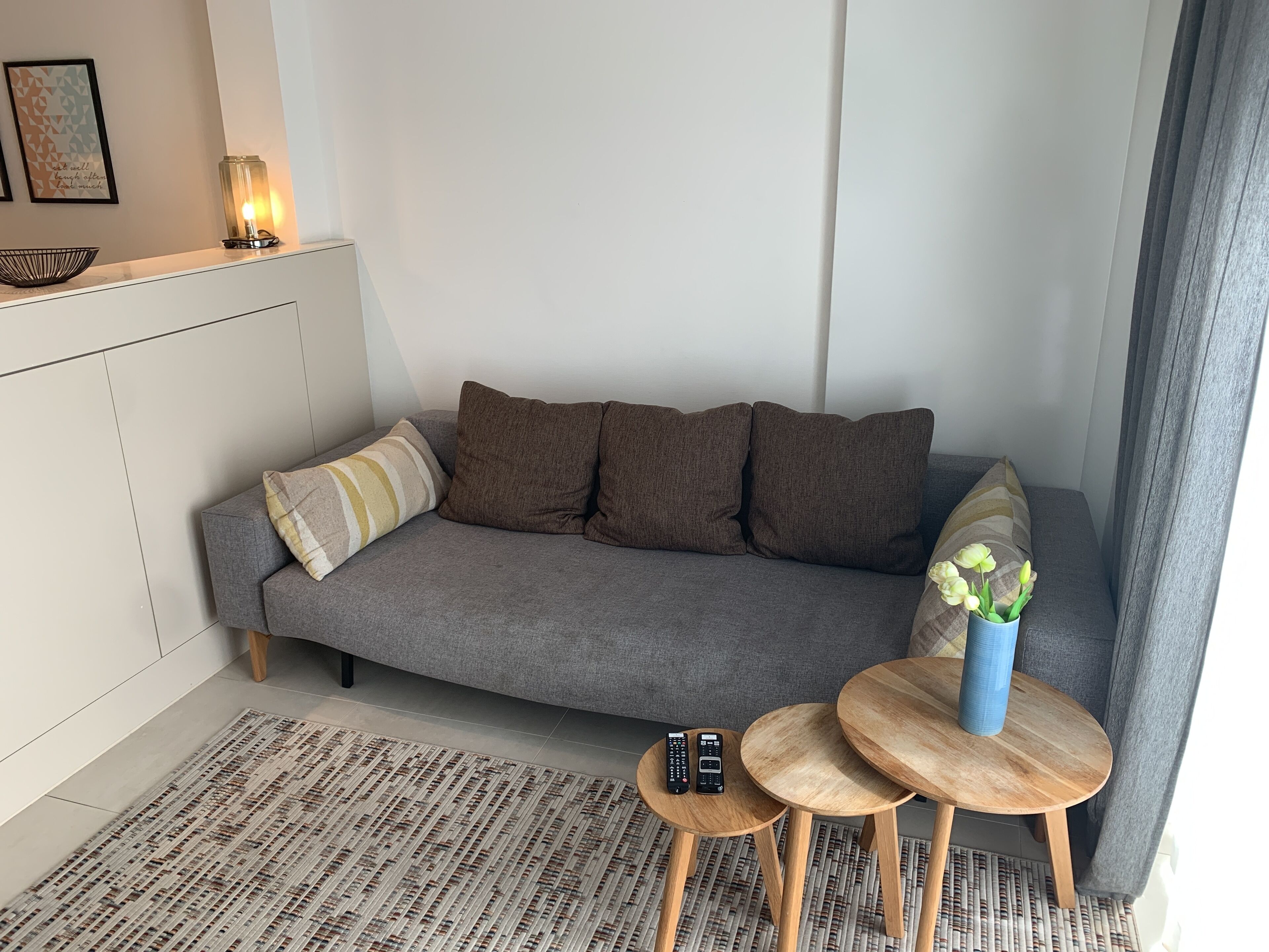 Ett modernt vardagsrum med en grå soffa, ett litet träbord och en vas med blommor.