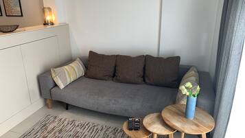 Ett modernt vardagsrum med en grå soffa, ett litet träbord och en vas med blommor.