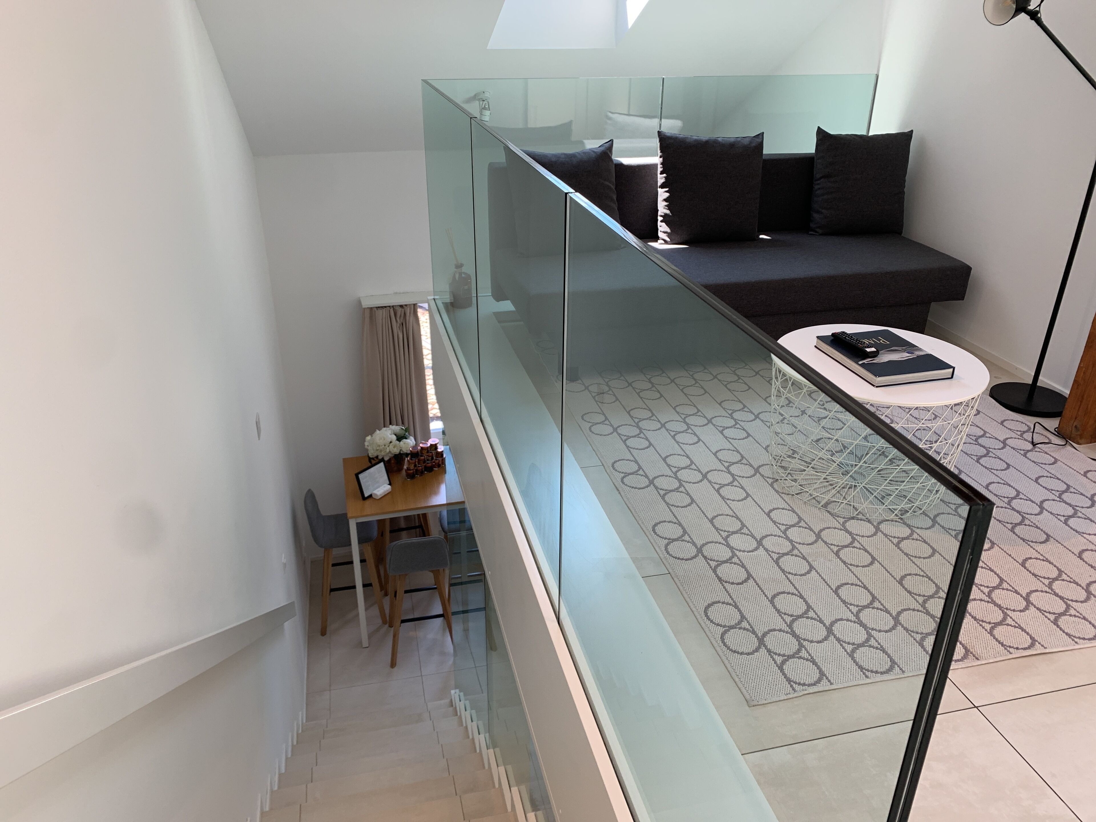 Un espacio de estar moderno con barandilla de vidrio, un sofá, una mesa de centro y una zona de comedor con sillas y una mesa.