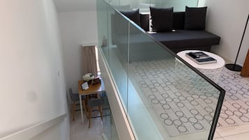 Un espacio de estar moderno con barandilla de vidrio, un sofá, una mesa de centro y una zona de comedor con sillas y una mesa.