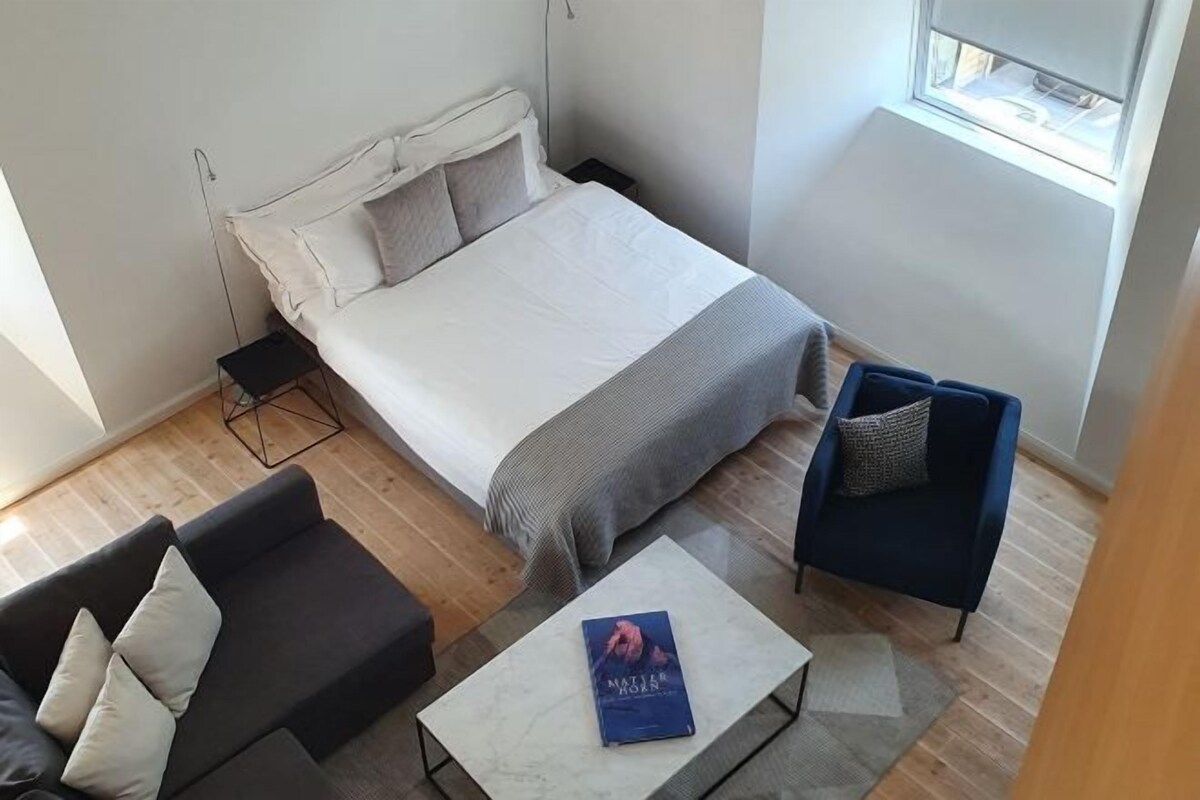A modern bedroom with a bed, a dark sofa, a small coffee table, and a window.