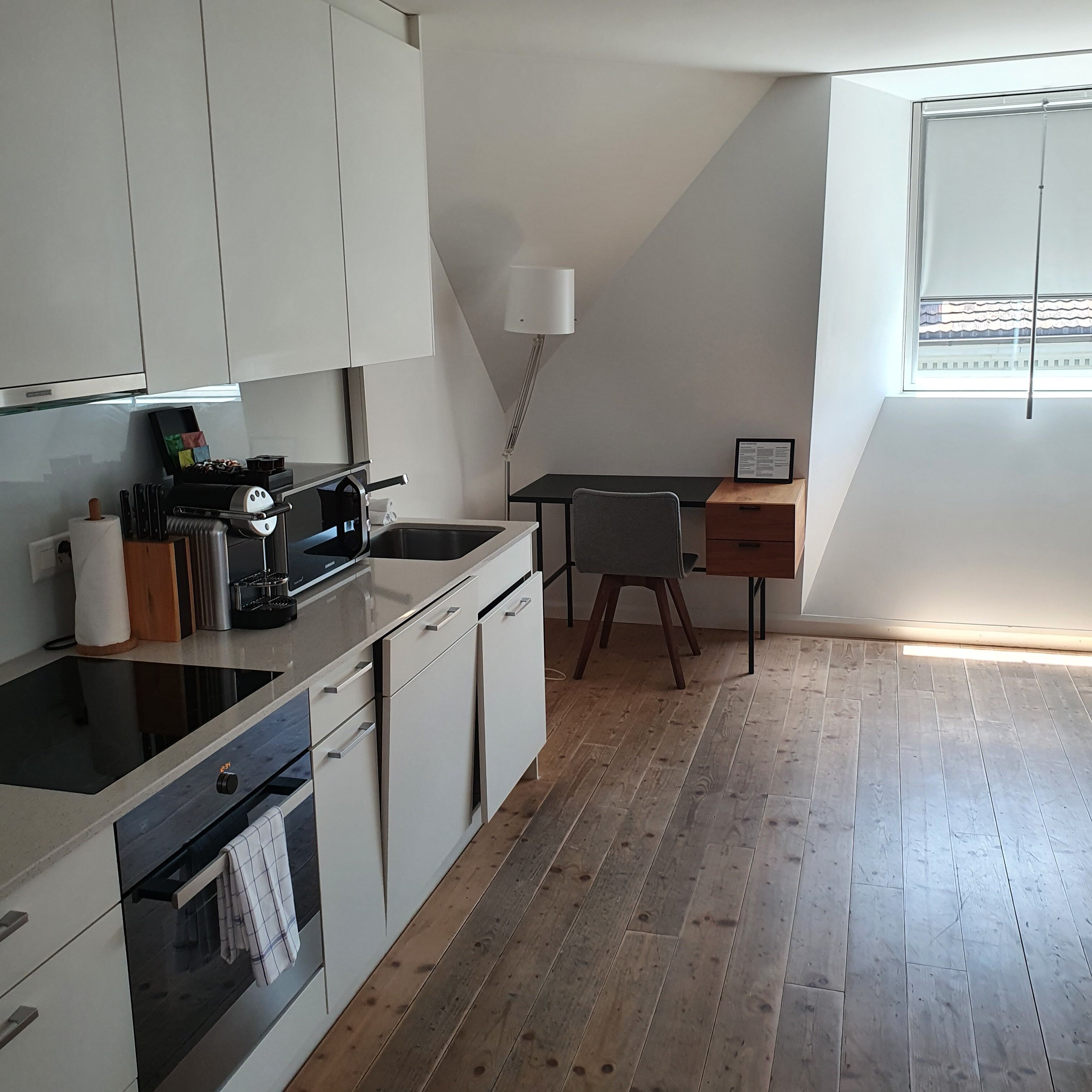 A compact kitchen with white cabinets, a black stove, and a wooden dining table with a chair.