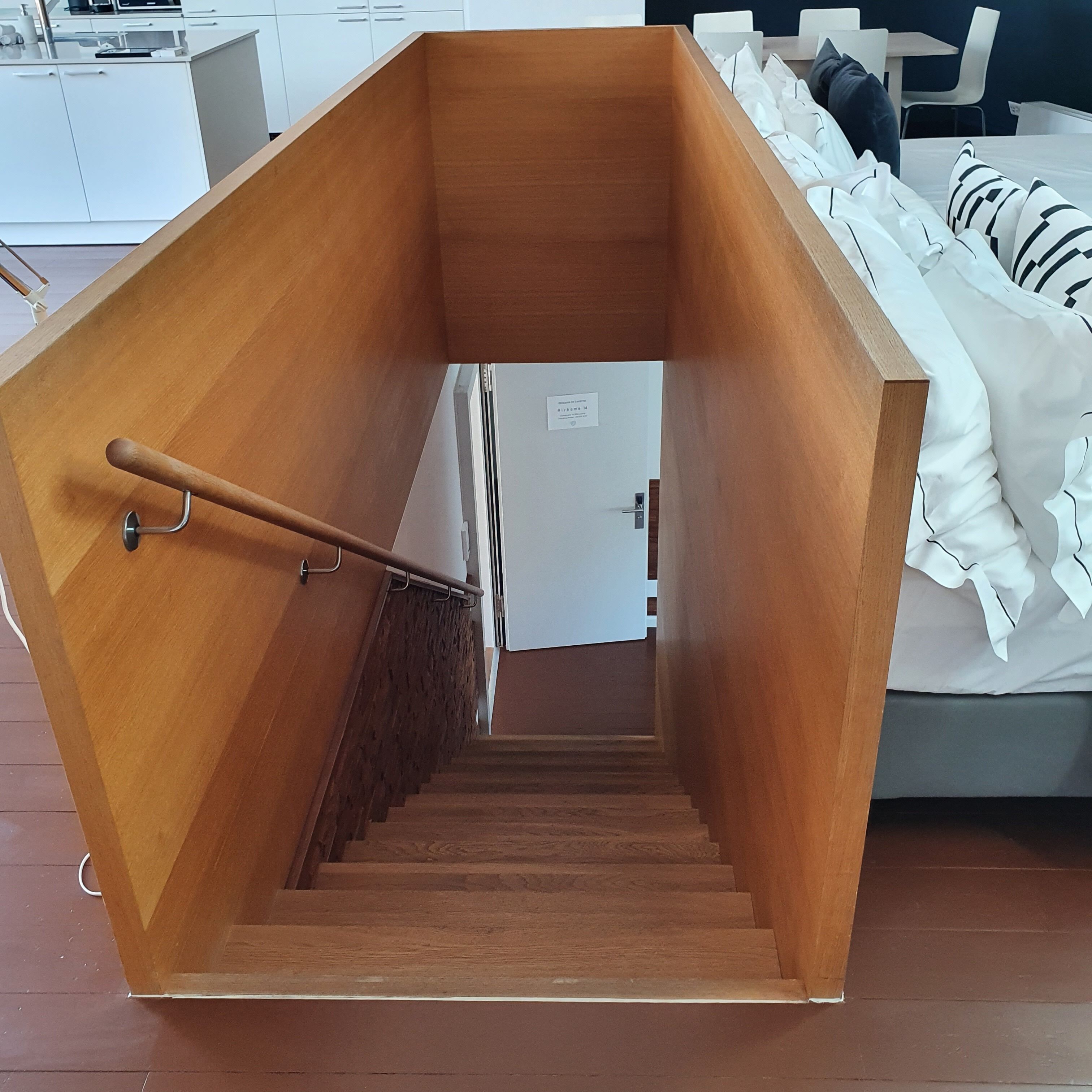 A wooden staircase leading to a bedroom with a bed and pillows.