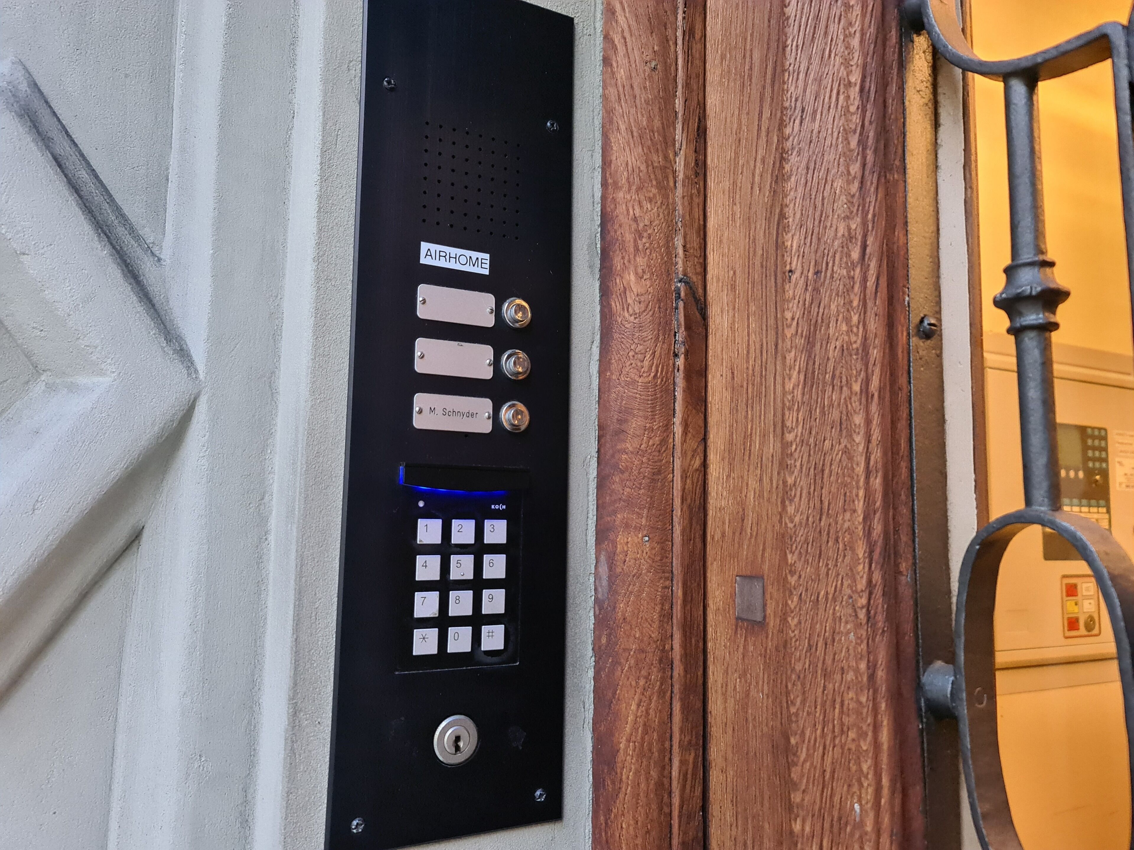 A black security keypad with a numeric keypad and a lock, mounted on a wall next to a wooden door.