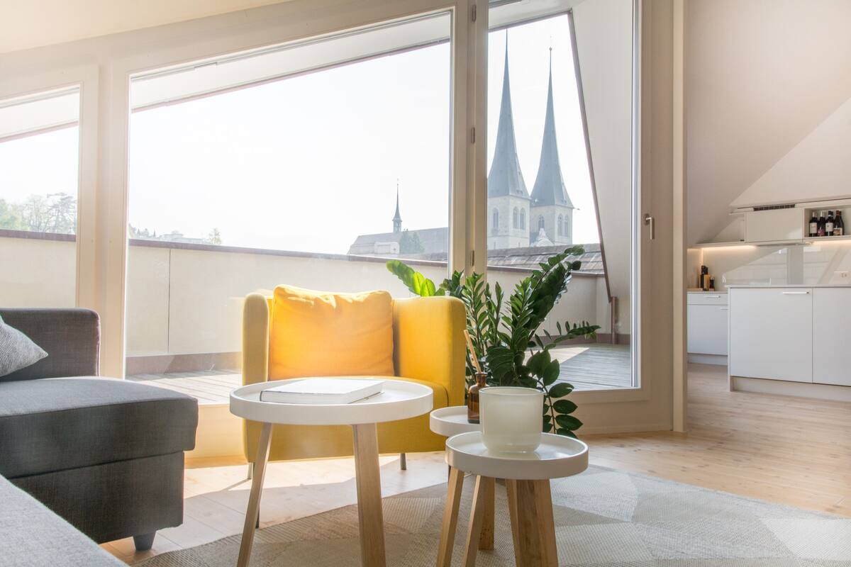 Una sala moderna con un sofá, un sillón amarillo, una mesita y una planta en maceta.