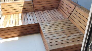 En träbänk med ett ribbmönster, placerad på en balkong med ett metallräcke.