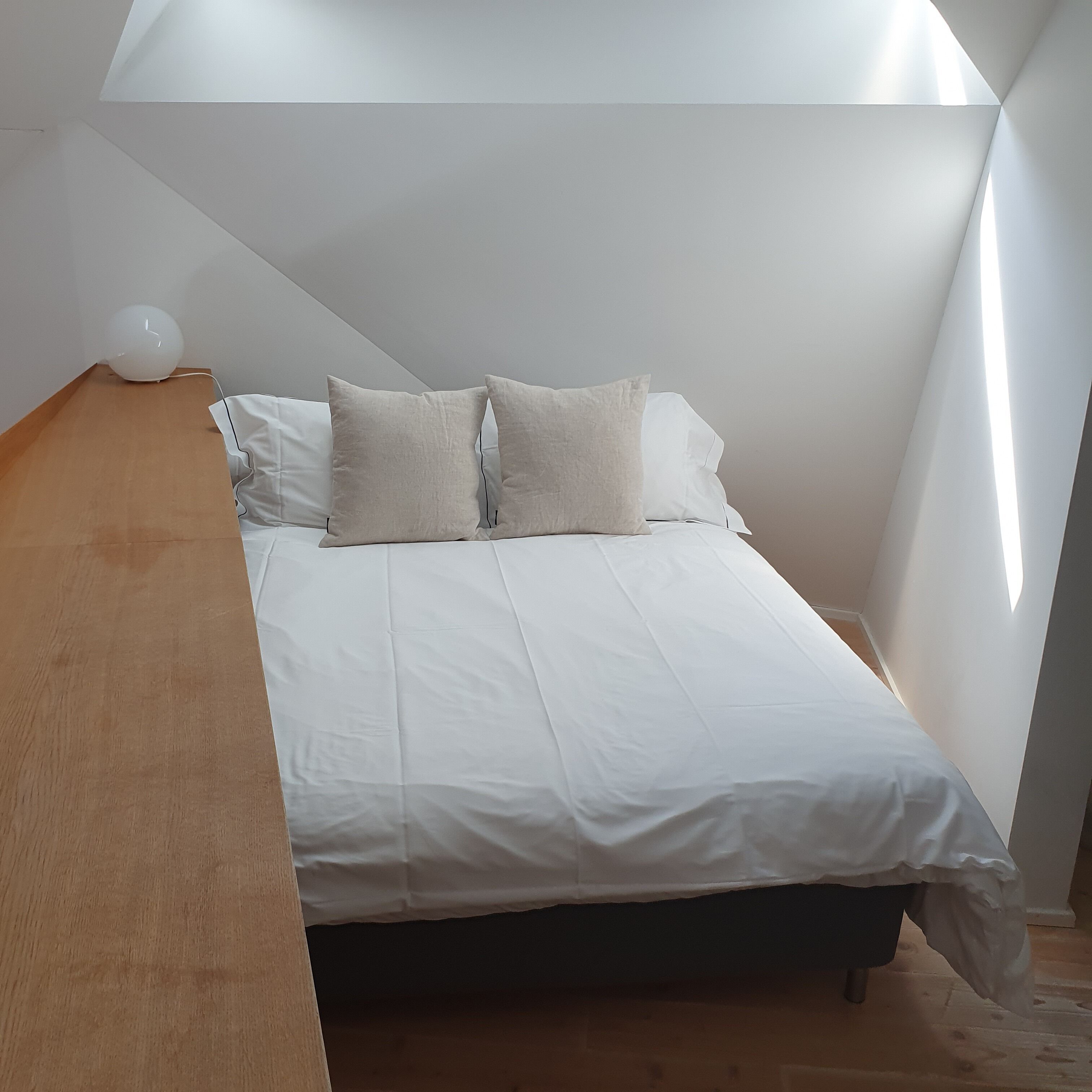 A bedroom with a bed, pillows, a wooden bench, and a white spherical object.