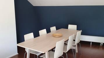 Une salle de conférence avec une longue table, des chaises blanches et un tableau en bois.