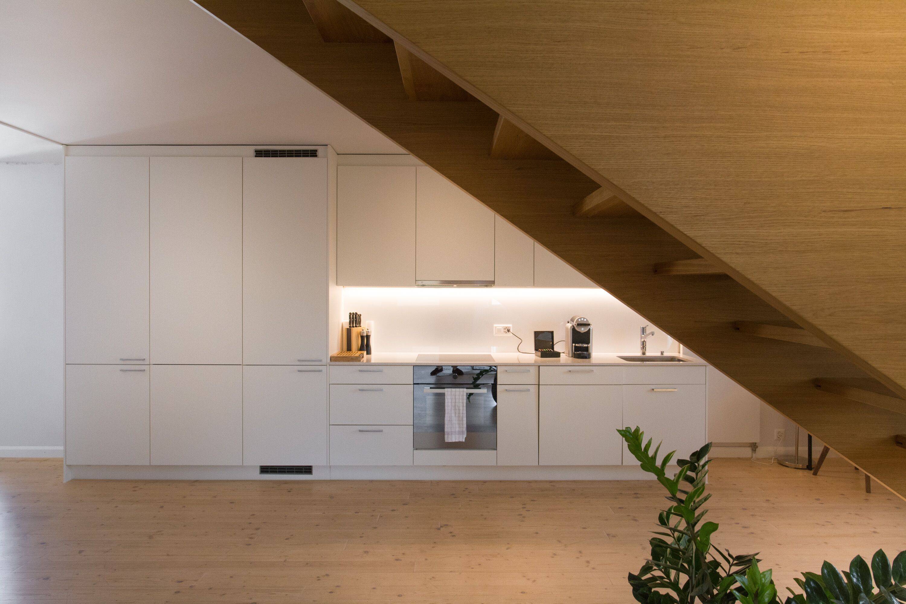 A modern kitchen with white cabinets, a stainless steel oven, and a wooden ceiling.