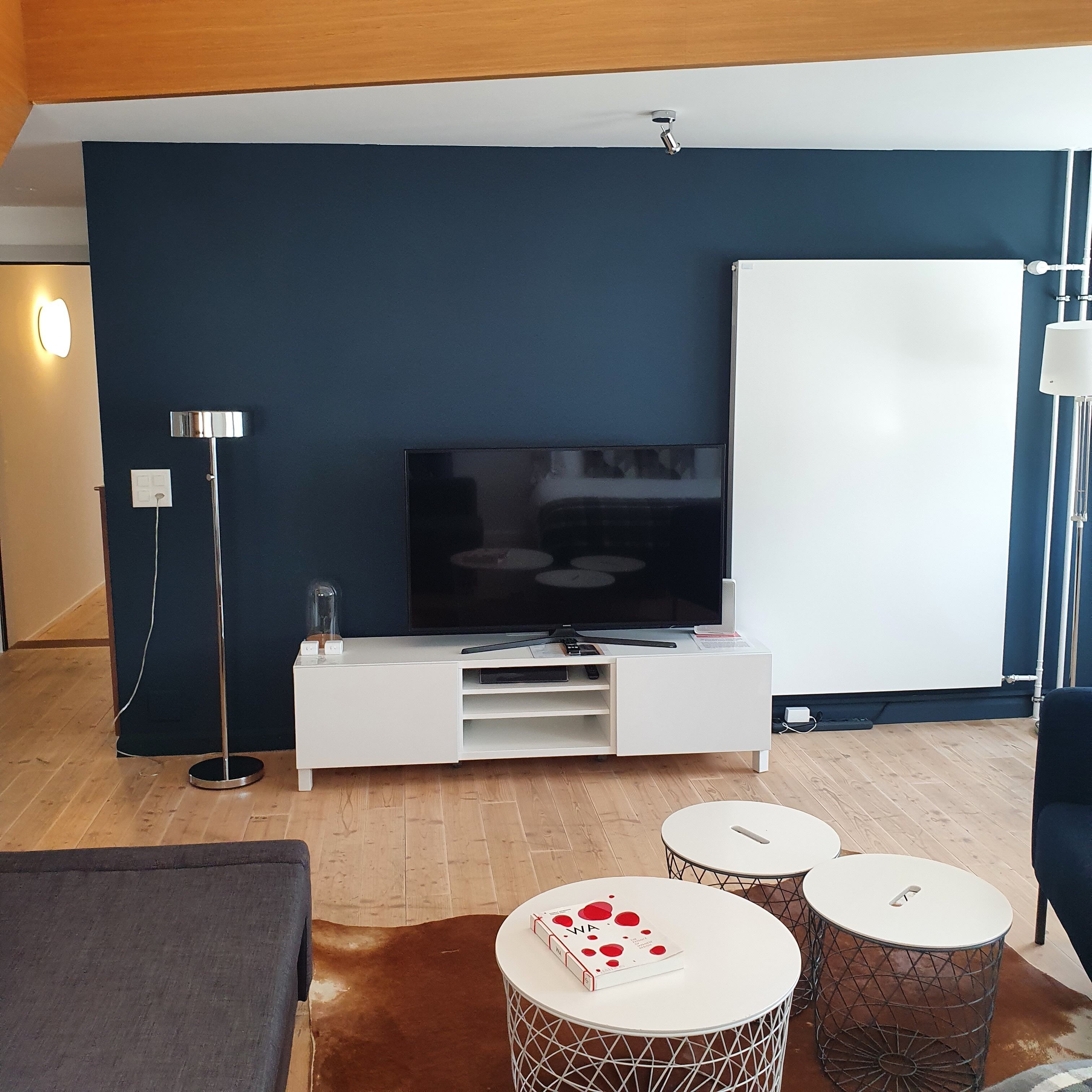 Un salon moderne doté d’un téléviseur à écran plat, d’un meuble de rangement blanc, de deux tables rondes, d’un canapé et d’une lampe.