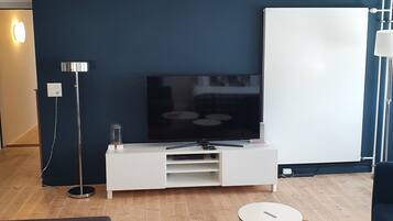 Un salon moderne doté d’un téléviseur à écran plat, d’un meuble de rangement blanc, de deux tables rondes, d’un canapé et d’une lampe.