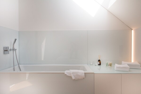 Un baño moderno con bañera vidriada, cabina de ducha de vidrio y tocador con artículos de aseo.