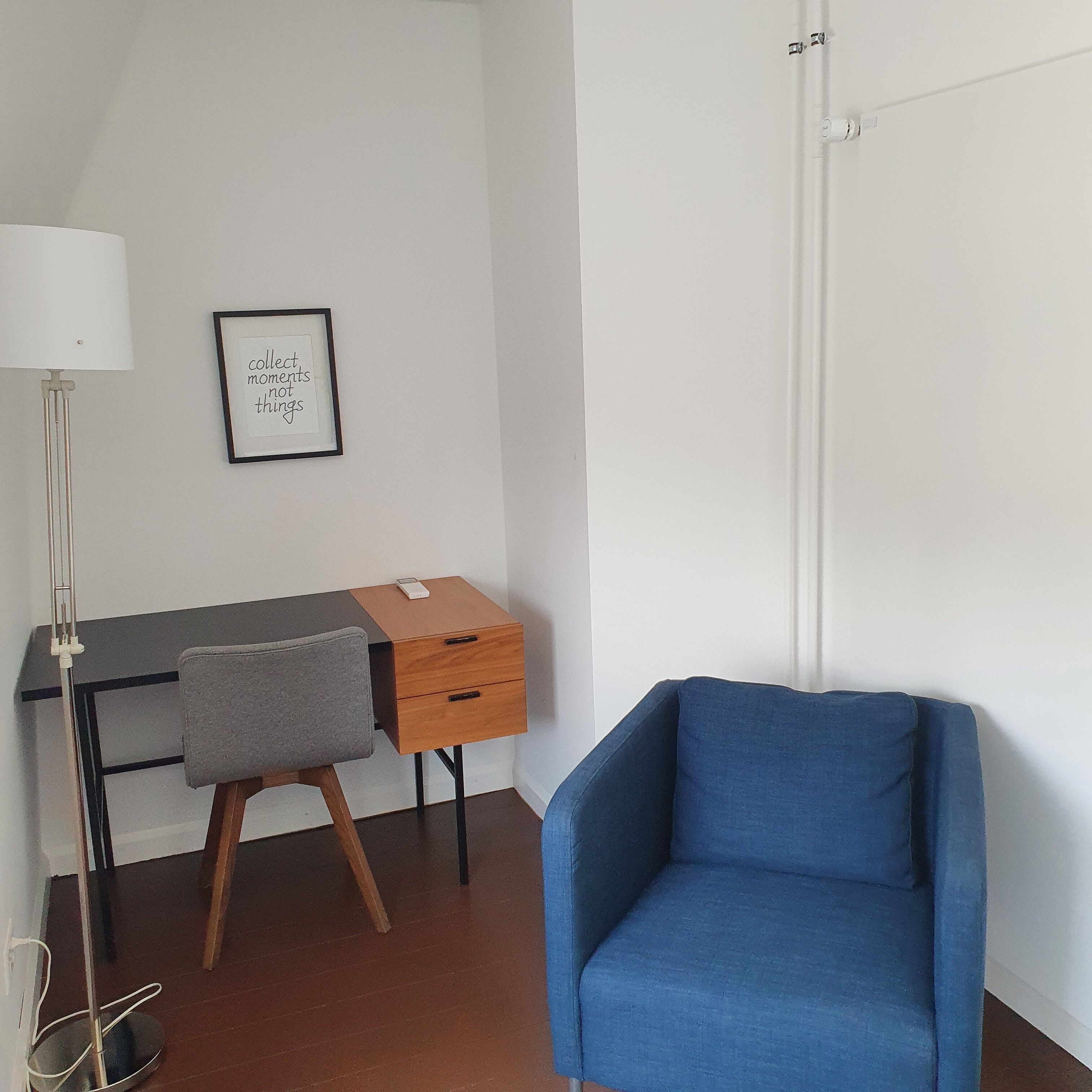 Una habitación con escritorio, silla, lámpara y una cita enmarcada en la pared.