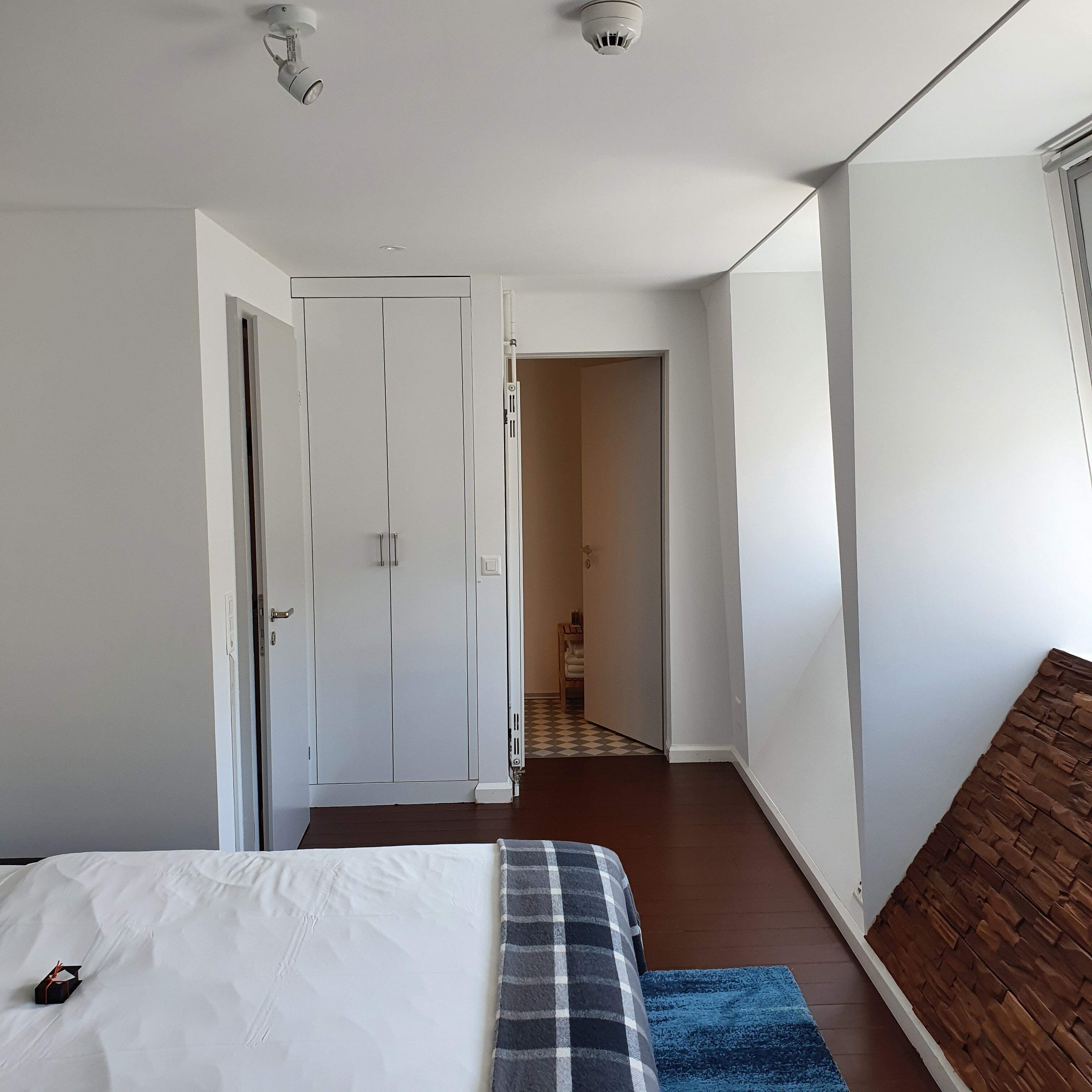Ein Schlafzimmer mit einem Bett, einem Kleiderschrank und einem durch eine offene Tür einsehbaren Badezimmer.