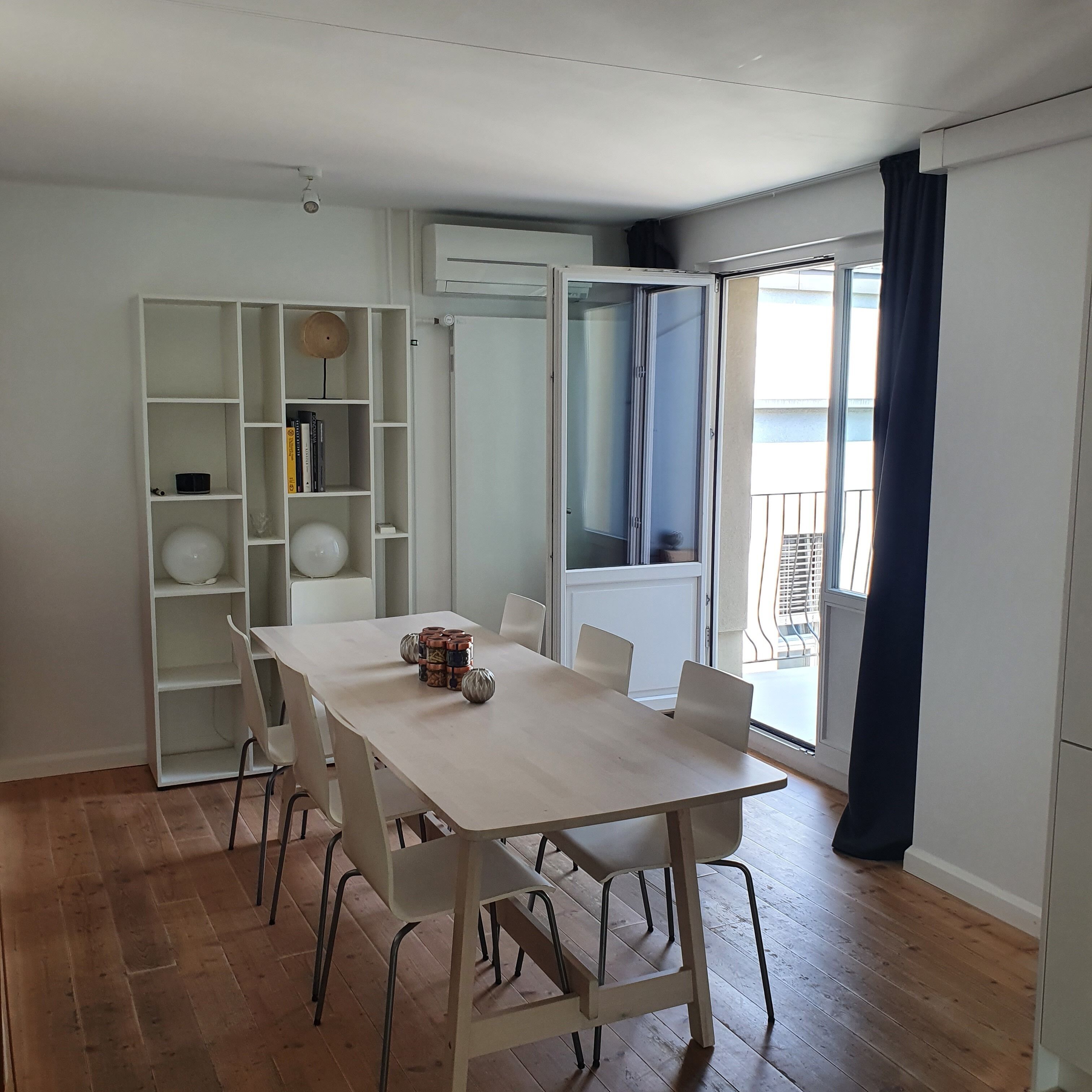Ein moderner Essbereich mit Holztisch und -stühlen, einer weißen Regaleinheit und Blick auf den Balkon.