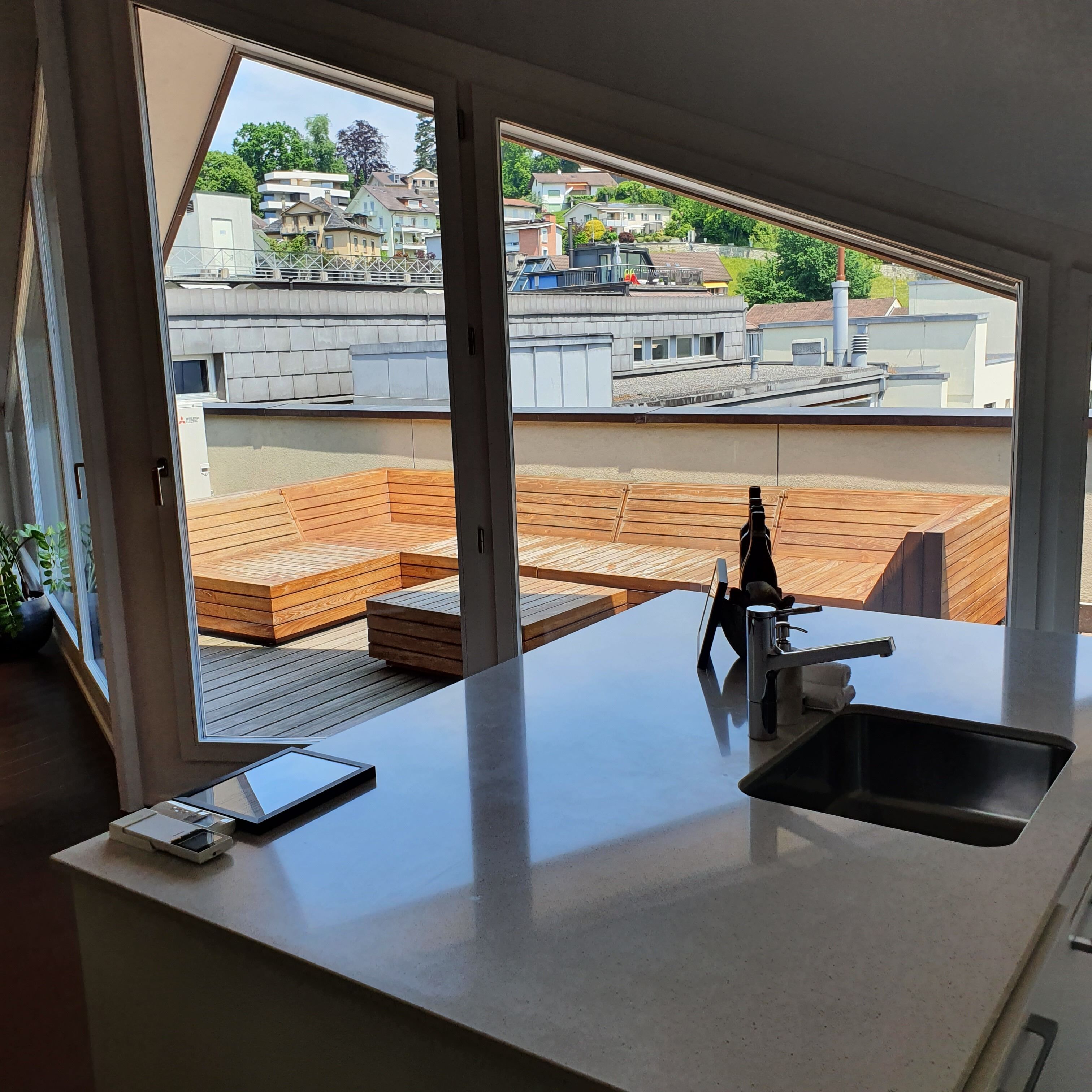 A modern kitchen with a large window, a built-in sink, and a wooden deck area visible through the window.