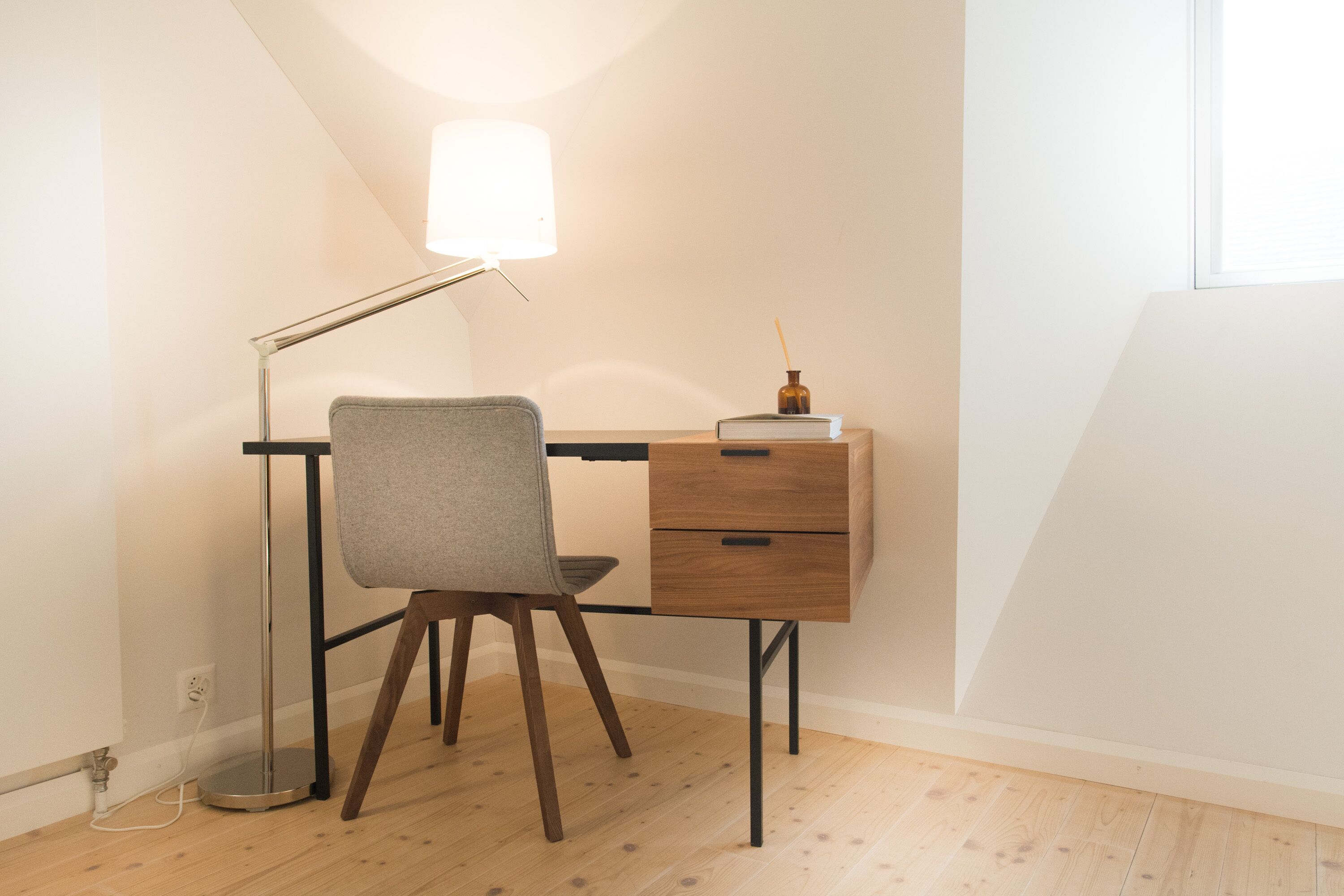 Een moderne werkruimte met een bureau, stoel, lamp en een klein decoratief object op het bureau.