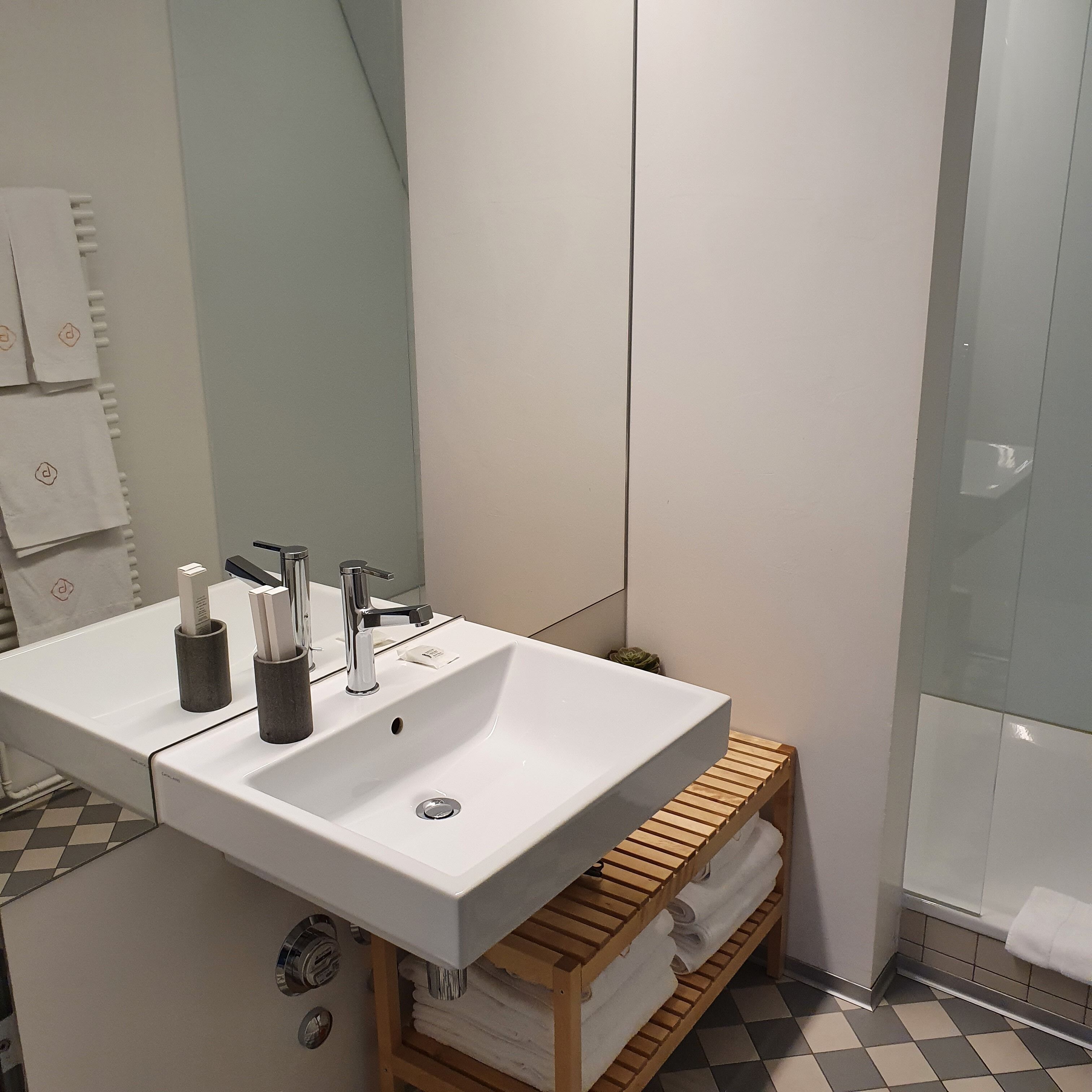 A bathroom with a white sink, two faucets, and a wooden towel rack.