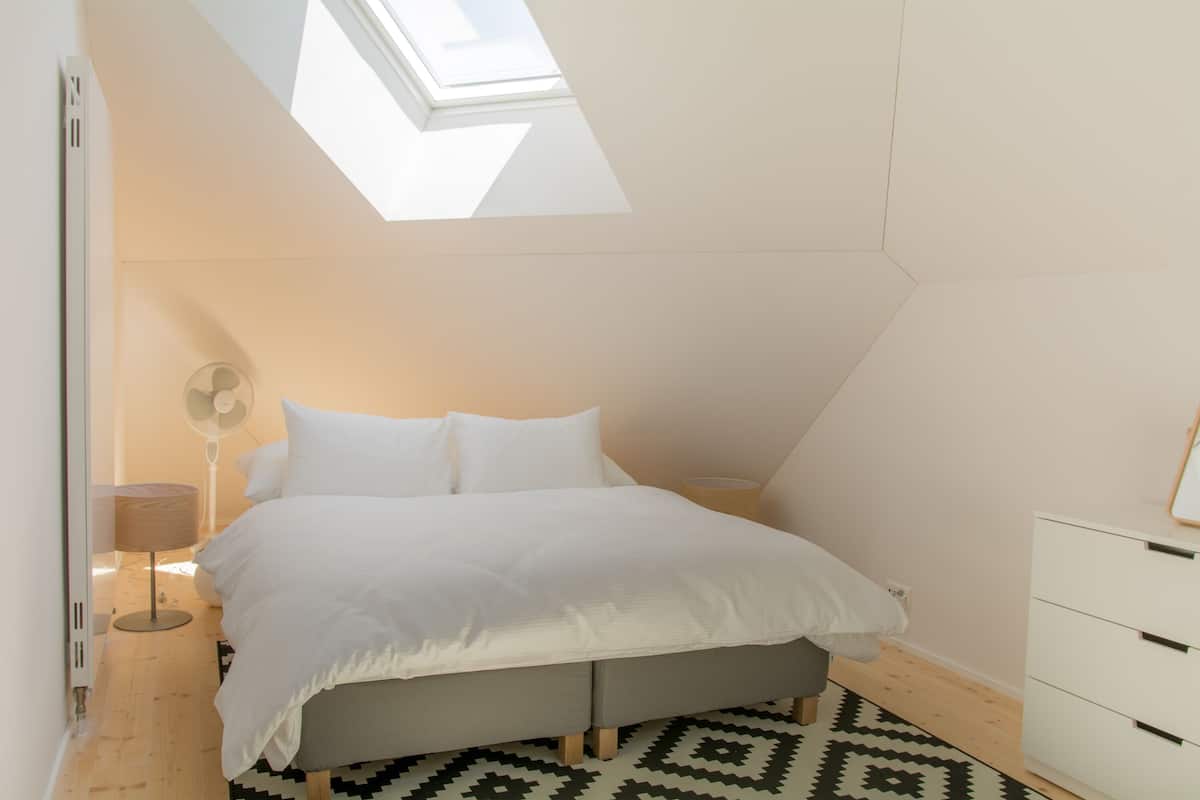 Un dormitorio con tragaluz, una cama, una mesita de noche, una lámpara y un aparador.