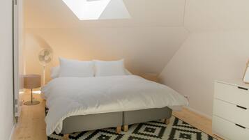 Un dormitorio con tragaluz, una cama, una mesita de noche, una lámpara y un aparador.
