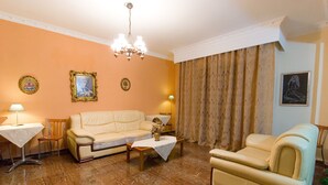Un soggiorno con un divano beige, un tavolino in legno, un piccolo tavolo con una lampada, una poltrona e un lampadario.