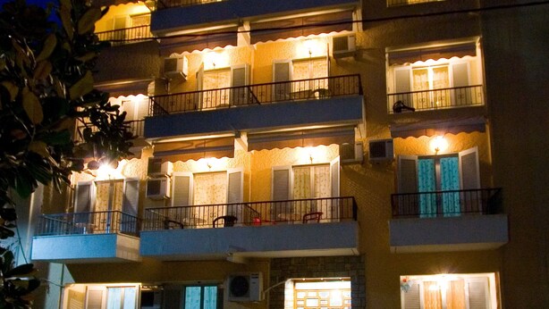 Un edificio a più piani con balconi, un ingresso centrale e piante in vaso in primo piano.