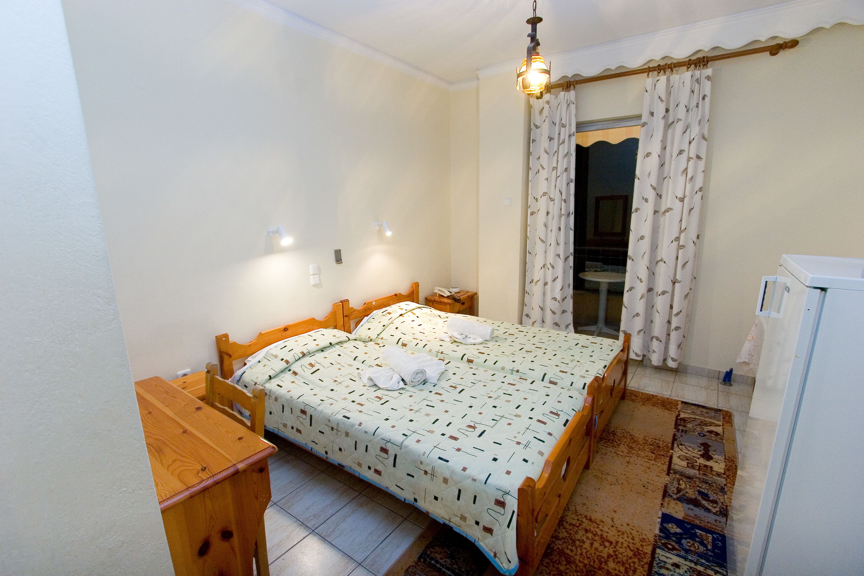 A bedroom with a bed, wooden furniture, a nightstand, a lamp, and a curtain.