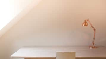A minimalist workspace with a desk and chair, a single desk lamp, and a sloped ceiling.