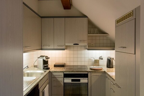 A compact kitchen with light-colored cabinets, a dishwasher, a coffee maker, and a kettle. - Airhome Zug Neugasse Stadtzentrum (Zug)