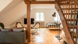 Une pièce de style loft avec un escalier en bois, un canapé, deux fauteuils, une petite table et un lit.