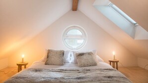 Une chambre mansardée chaleureuse, avec un plafond en pente, un puits de lumière, un lit agrémenté de coussins moelleux et deux lampes de chevet.