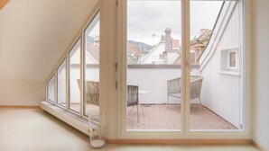 Une pièce dotée d’une grande porte-fenêtre coulissante qui donne sur un patio extérieur avec un sol en briques et deux fauteuils en osier.