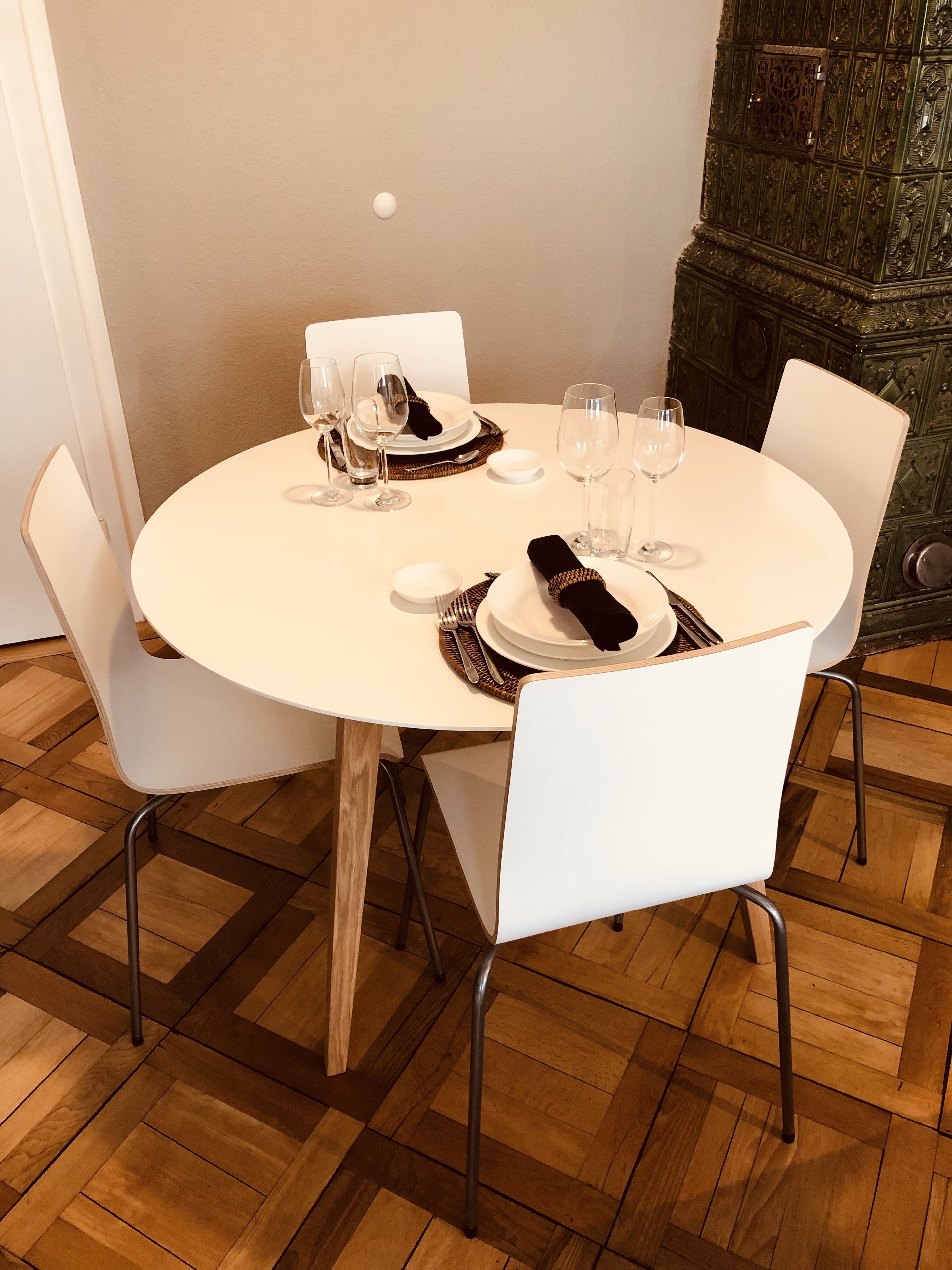 Et rundt spisebord med hvide stole, dækket med tallerkener, glas og bestik.