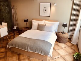 Un dormitorio ordenado con una cama grande, una silla, una mesita, una lámpara, un cuadro enmarcado y un radiador.