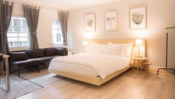Habitación de hotel con una cama grande, un sofá y un escritorio. Hay tres cuadros en la pared.
