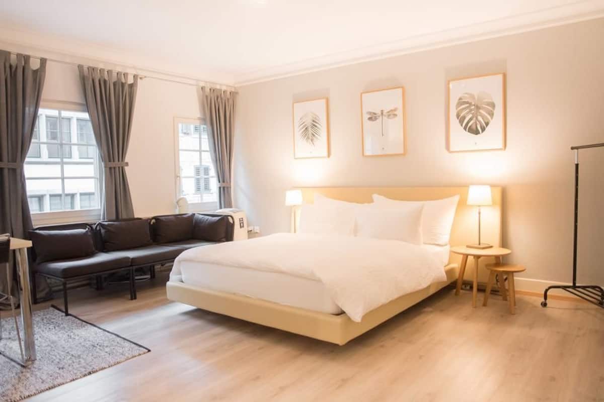 A hotel room with a large bed, a sofa, and a desk. There are three framed pictures on the wall.