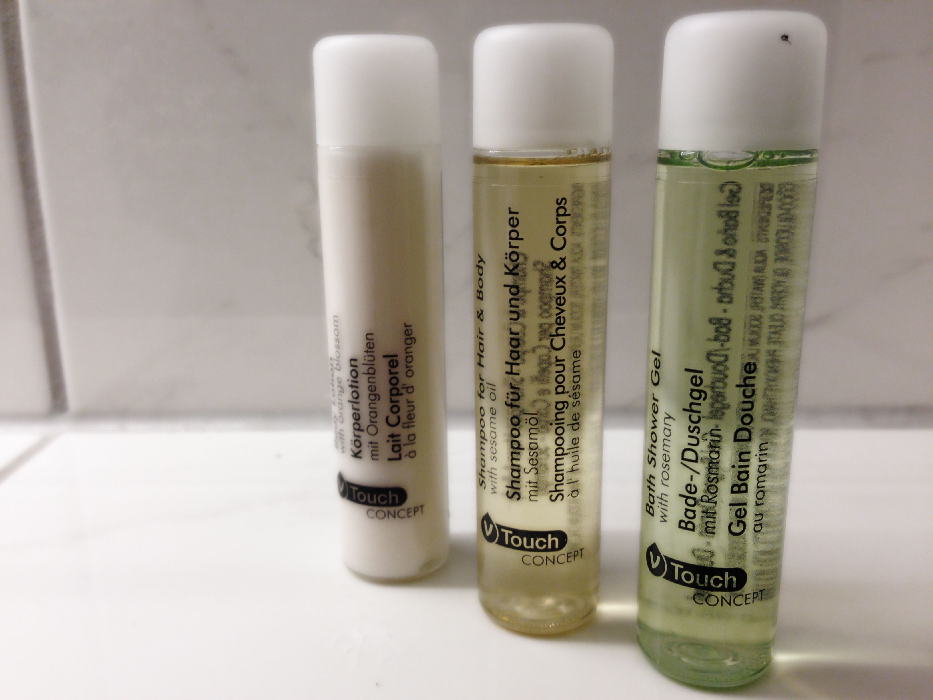 Três frascos de produtos para cabelo e corpo Touch Concept sobre uma superfície branca.