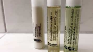 Três frascos de produtos para cabelo e corpo Touch Concept sobre uma superfície branca.