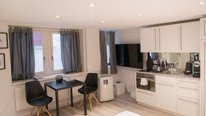 Una cocina moderna con armarios blancos, horno empotrado y cafetera. Cuenta con una zona de comedor con mesa y sillas, además de un ventanal con cortinas.