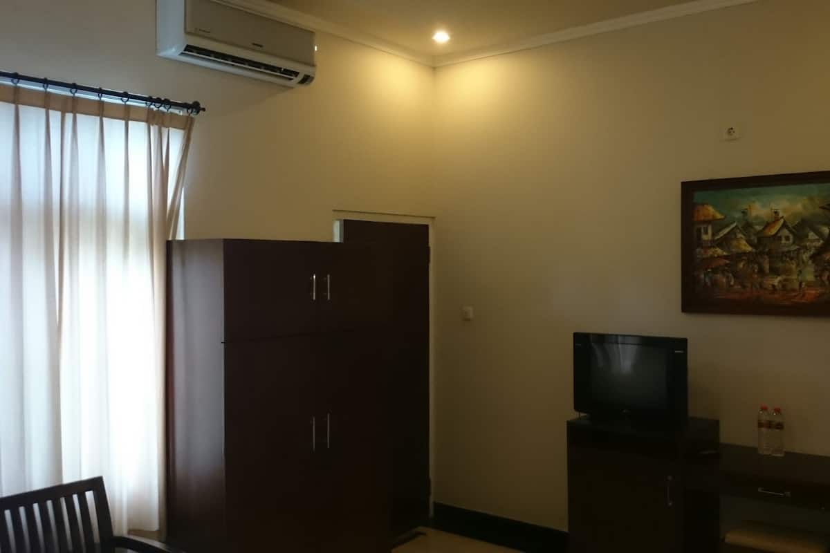A room with a dark wooden wardrobe, a flat-screen TV on a small cabinet, and a painting on the wall.