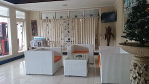 Una sala moderna con muebles de mimbre blanco, una planta grande en maceta y un televisor montado en la pared.