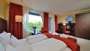 A hotel room with two beds, a TV, a desk, and a view of greenery outside. - ARIBO Hotel Erbendorf (Erbendorf)
