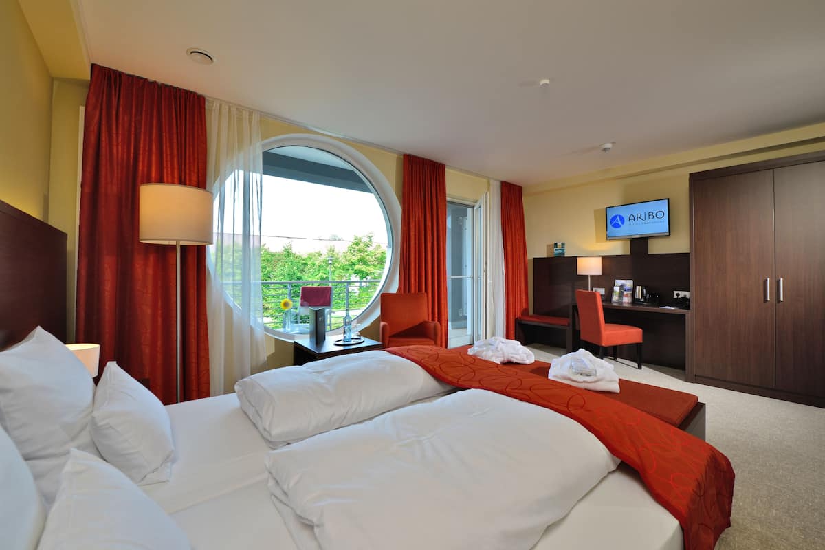 Une chambre d’hôtel avec deux lits, une télévision, un bureau et une vue sur la verdure environnante.