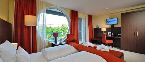 Quarto de hotel com duas camas, televisão, escrivaninha e vista para o verde lá fora.