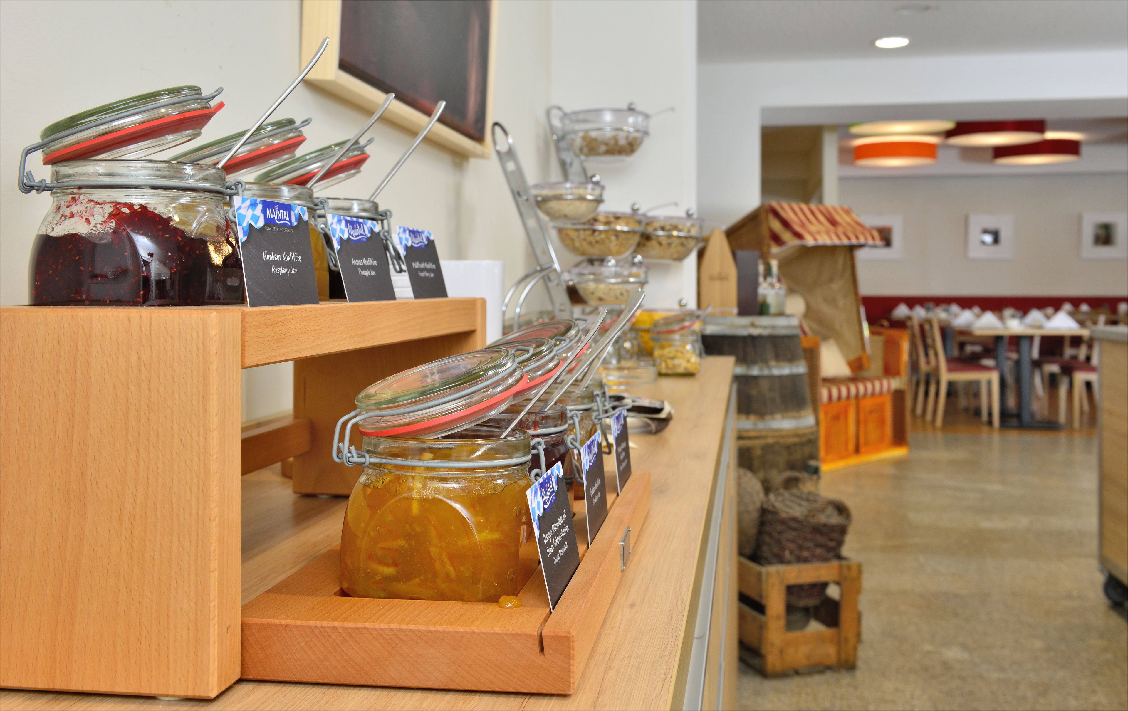 A buffet setup with various food items in jars and bowls, wooden serving boards, and a seating area in the background.