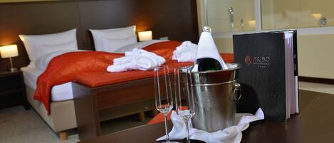 A hotel room with a neatly made bed, a minibar, and two glasses of champagne on the table.