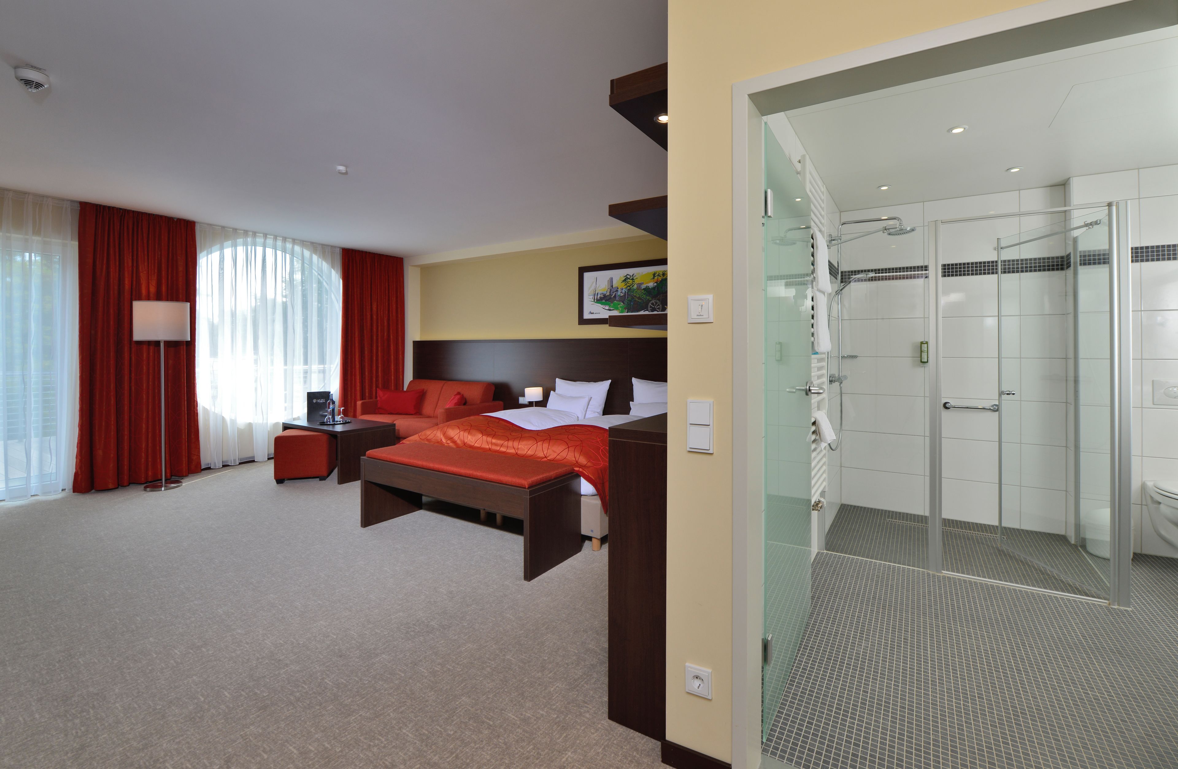 Une chambre d’hôtel comprenant un lit, un bureau, une chaise, un canapé, une douche en verre et une grande fenêtre avec des rideaux.