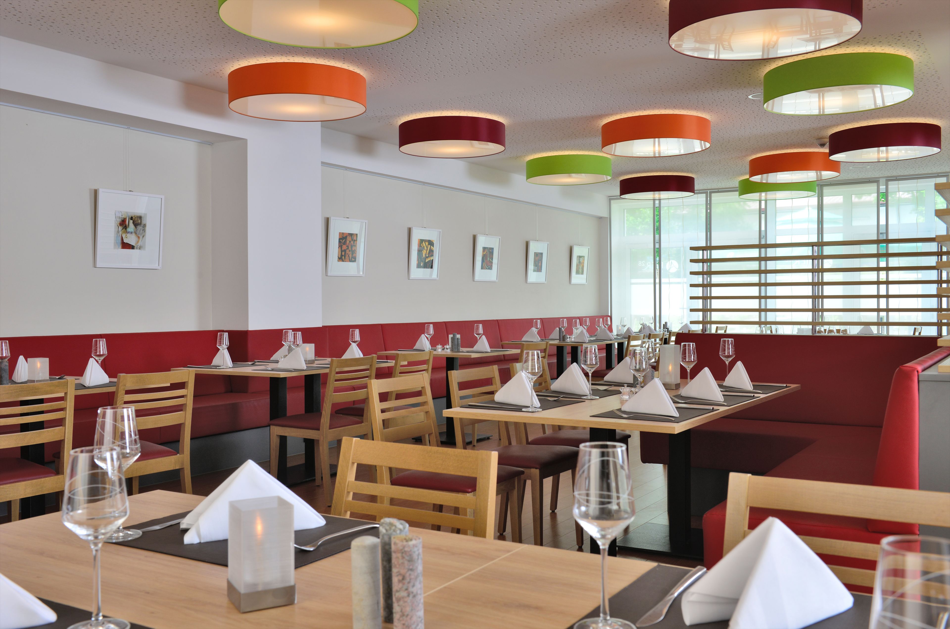 Ein Restaurant mit Holztischen und roten, gepolsterten Sitzbänken, mit hängenden Pendelleuchten und gerahmten Kunstwerken an den Wänden.