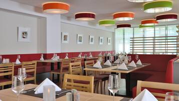 Ein Restaurant mit Holztischen und roten, gepolsterten Sitzbänken, mit hängenden Pendelleuchten und gerahmten Kunstwerken an den Wänden.